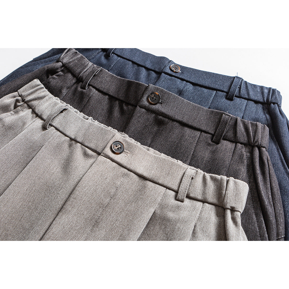 Close-up of gray, charcoal, and navy trousers showing buttoned waistbands and belt loops.