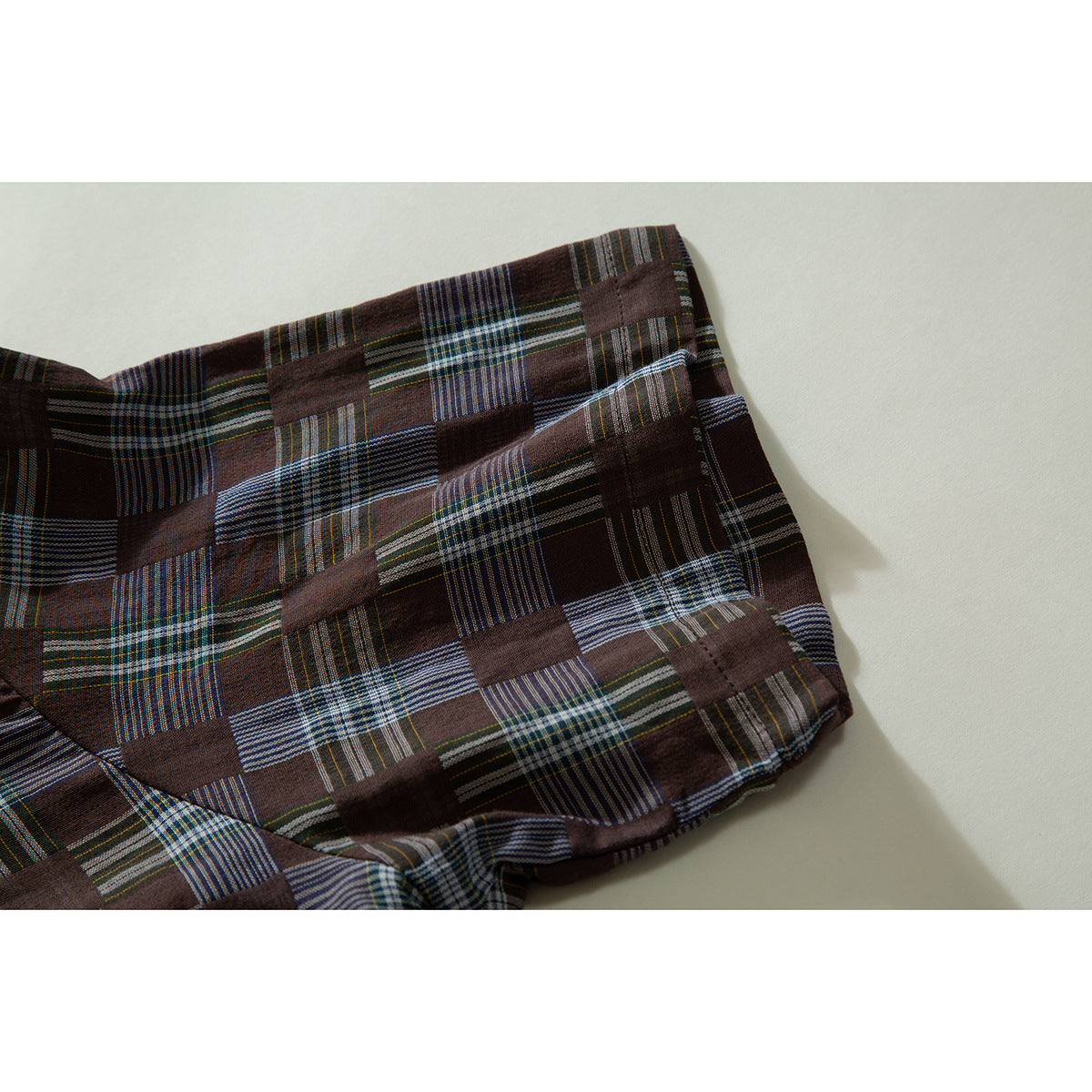 Close-up of the brown patchwork-plaid shirt's folded sleeve and stitched edge.