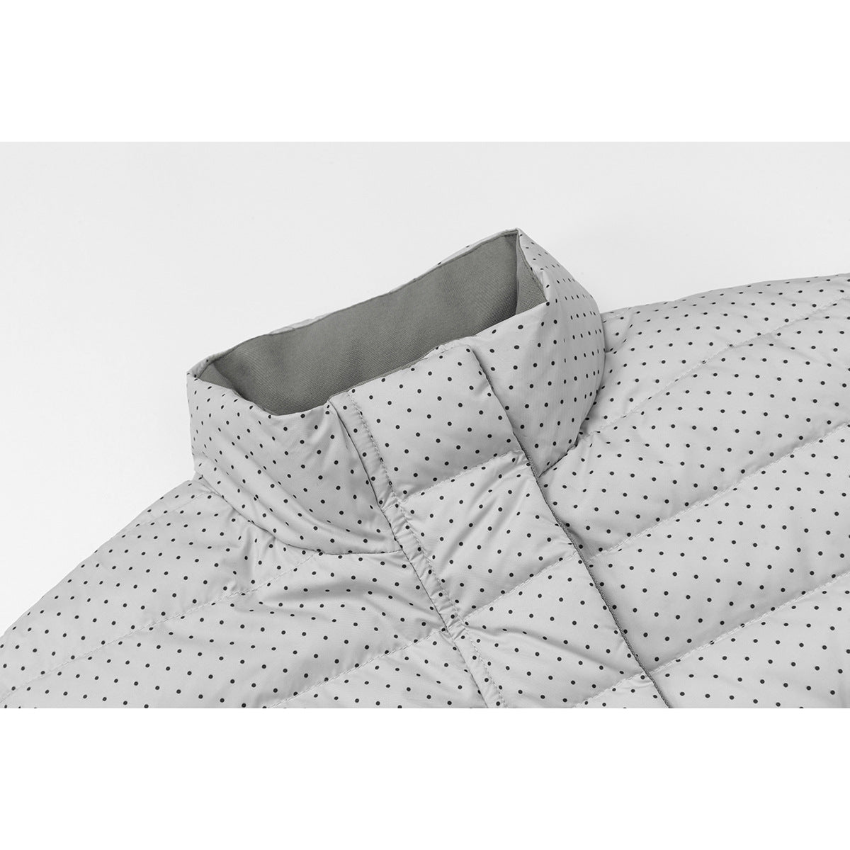 Close-up of a light gray quilted jacket with black polka dots, showing its high collar and front placket.
