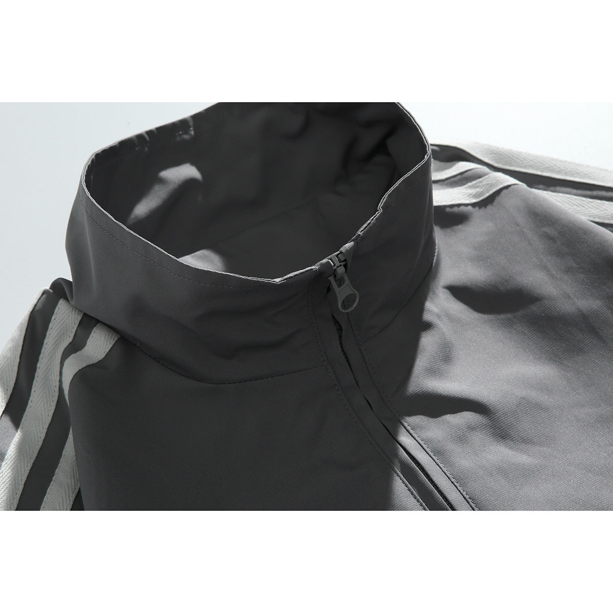 Close-up of a charcoal track jacket's stand collar, front zipper pull, and white shoulder stripes.