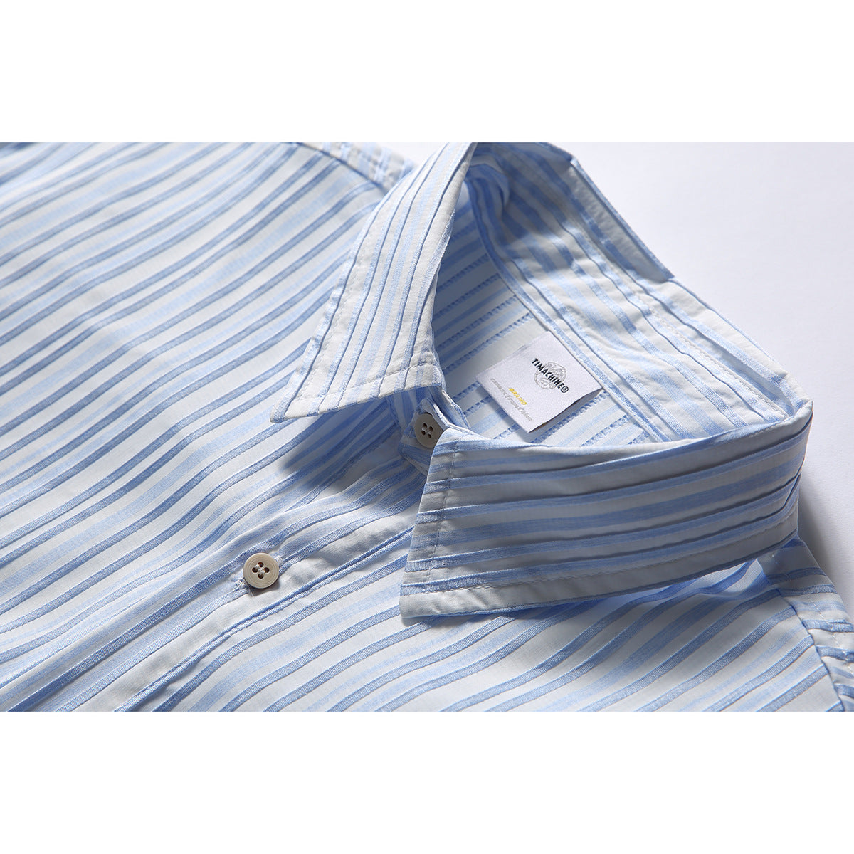 Close-up of a white shirt with pale blue vertical stripes, showing the open collar, buttons, and inner label.