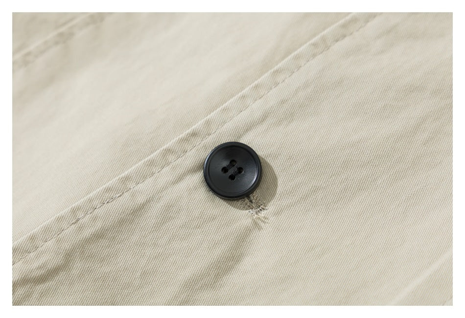Close-up of a black four-hole button and stitching on pale beige fabric.