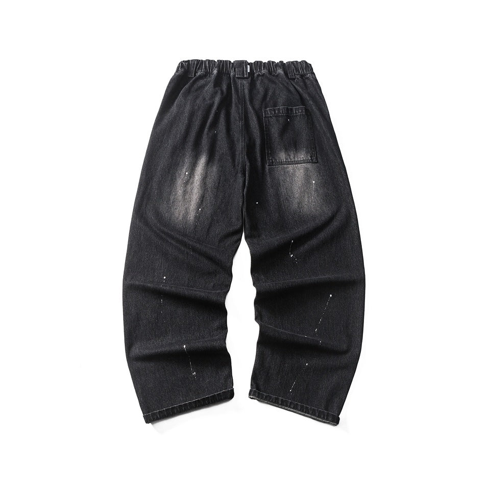 Back of black washed denim jeans with elastic waistband section, patch pocket and white paint splatters