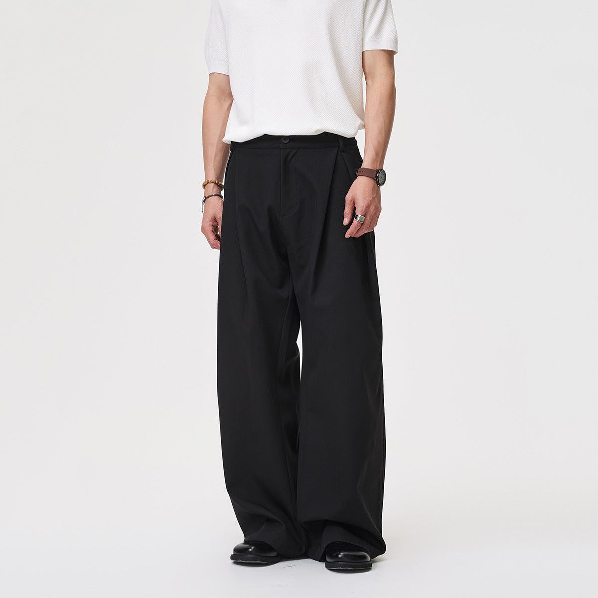 Model wearing black, pleated wide-leg trousers with a long, loose fit, shown from the front.