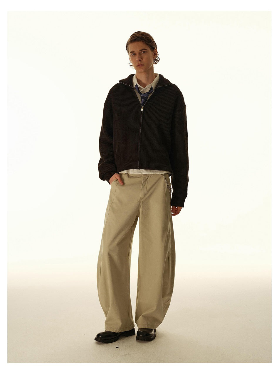 Model wearing a dark ribbed zip-front sweater with a high collar, layered over a shirt and tie.