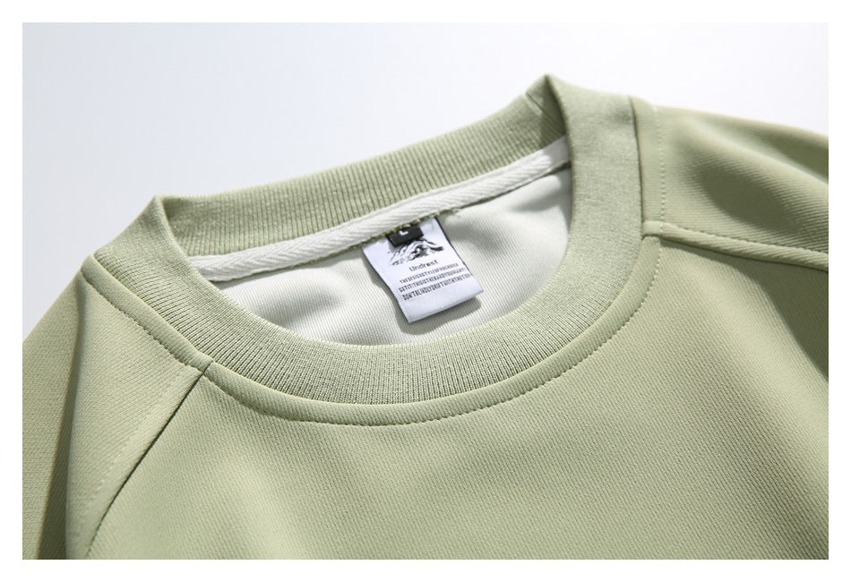 Close-up of a sage-green sweatshirt’s ribbed crew neckline and sewn-in neck label.