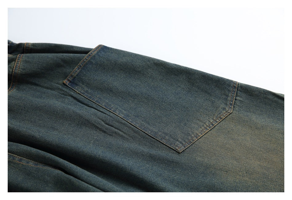 Close-up of dark indigo denim trousers showing a large patch pocket with brown contrast stitching.