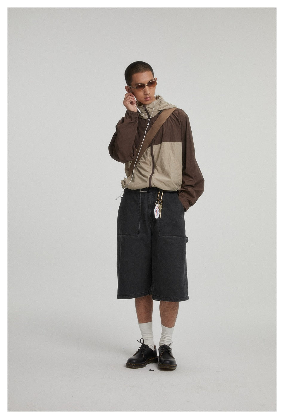 Model wearing a brown and beige color-block hooded jacket with loose black denim shorts.