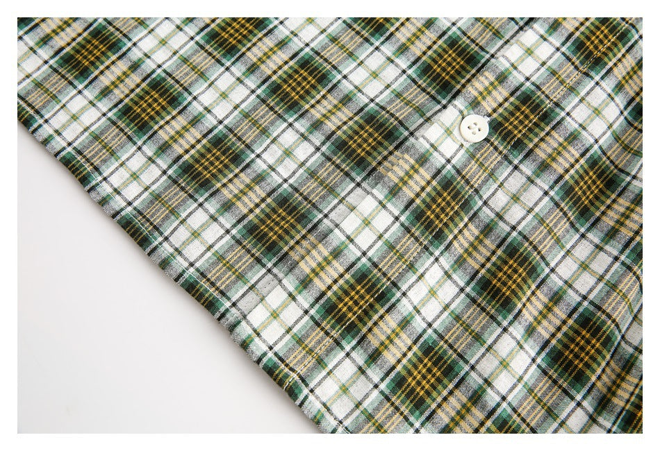 Close-up of a white, green, black, and mustard plaid shirt with a small white button.