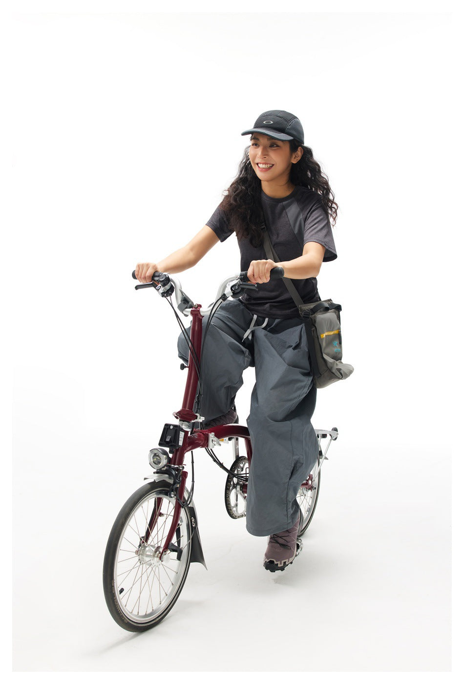 Model wearing a black cap, charcoal color-block T-shirt, and loose gray pants while seated on a bicycle.