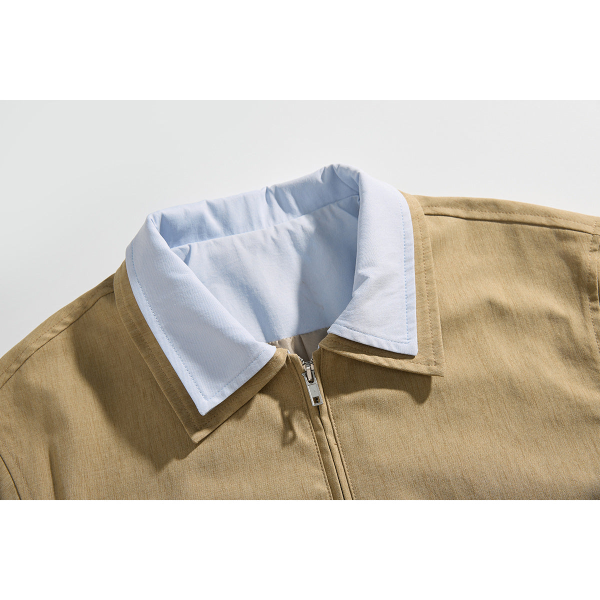 Close-up of a tan jacket with a pale blue pointed collar and front zipper.