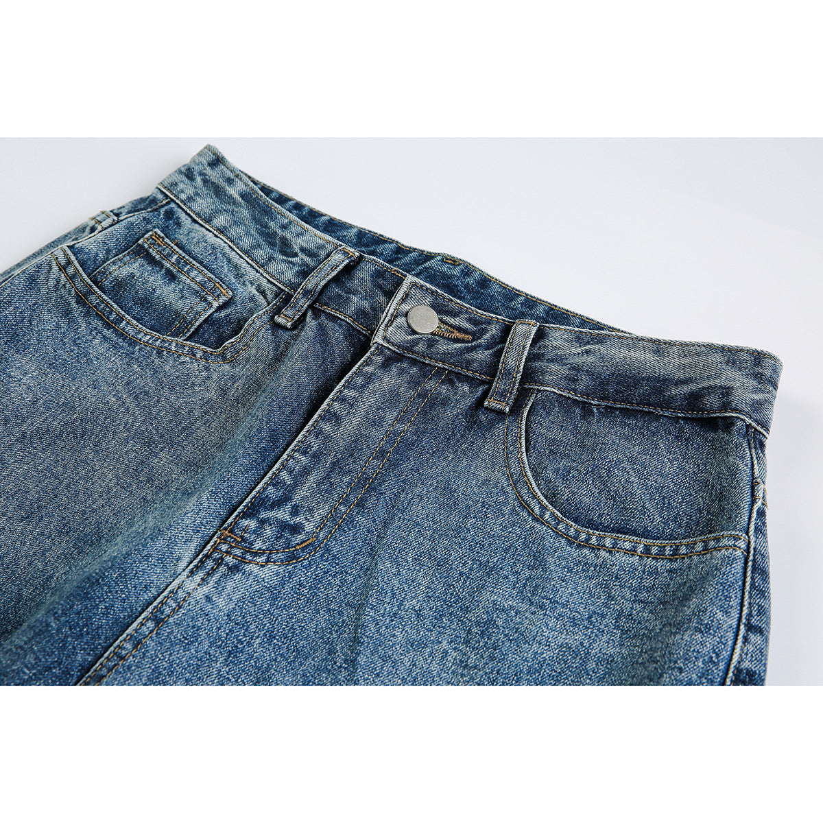 Close-up of blue acid-wash jeans showing the front waistband, button, belt loops and front pockets.
