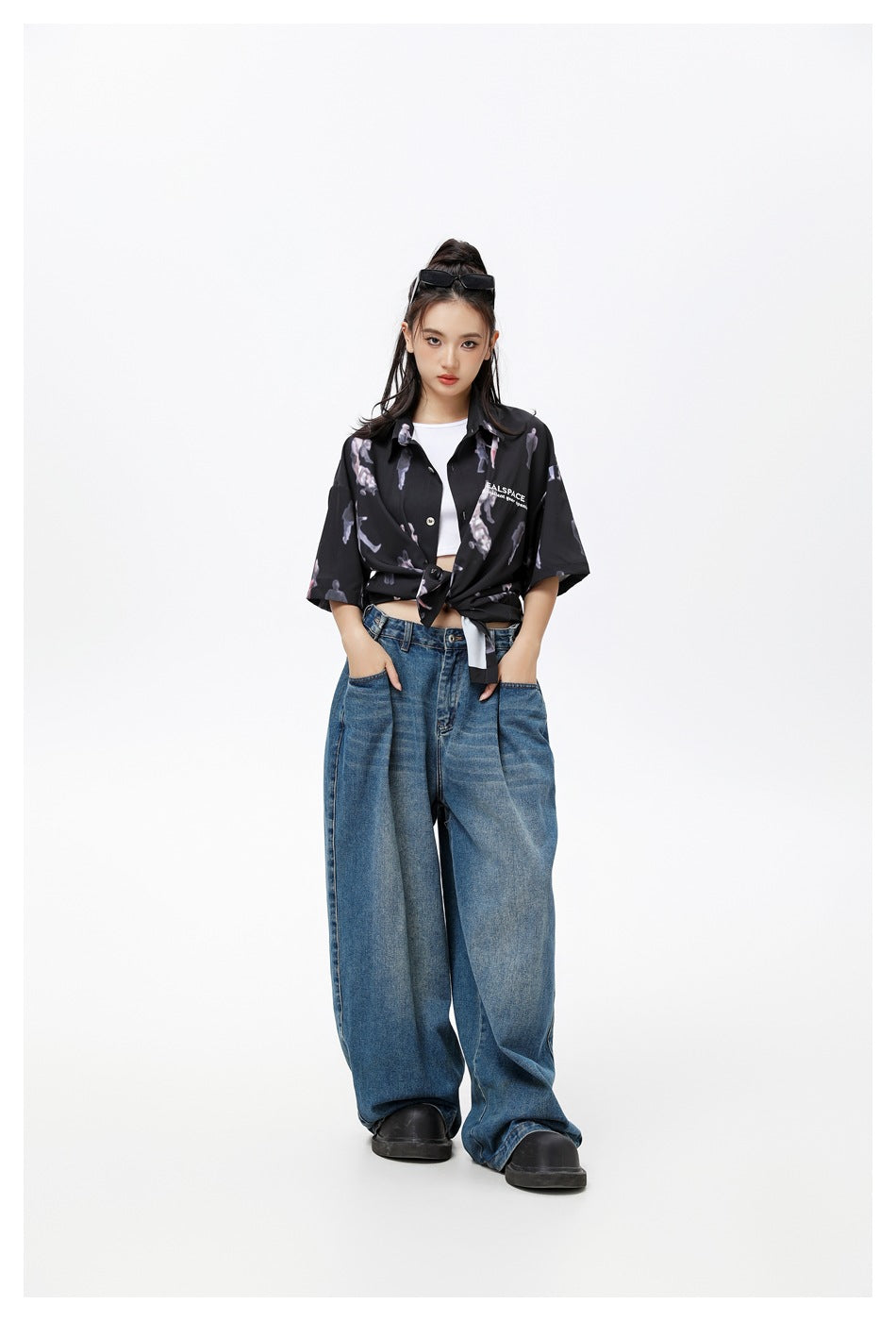 Model wearing black printed short-sleeve shirt knotted at the waist over a white top with baggy jeans