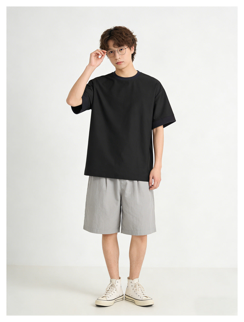 Model wearing a black short-sleeve T-shirt with subtle dark trim, paired with light gray shorts.