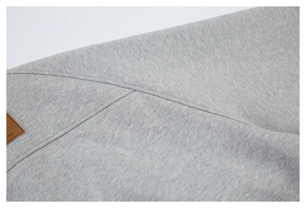 Close-up of gray knit garment fabric with intersecting seams and part of a brown label at the edge.