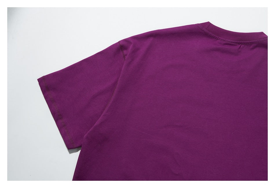 Angled close view of the back and sleeve of a plain purple shirt laid flat.