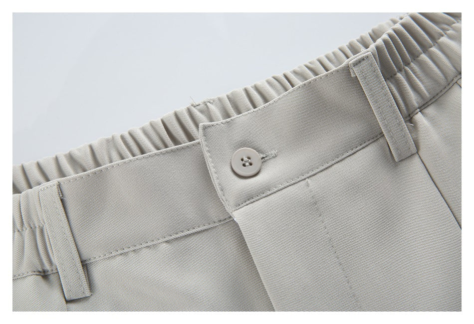 Close-up of light beige trousers showing an elasticated waistband, belt loops, button and fly.