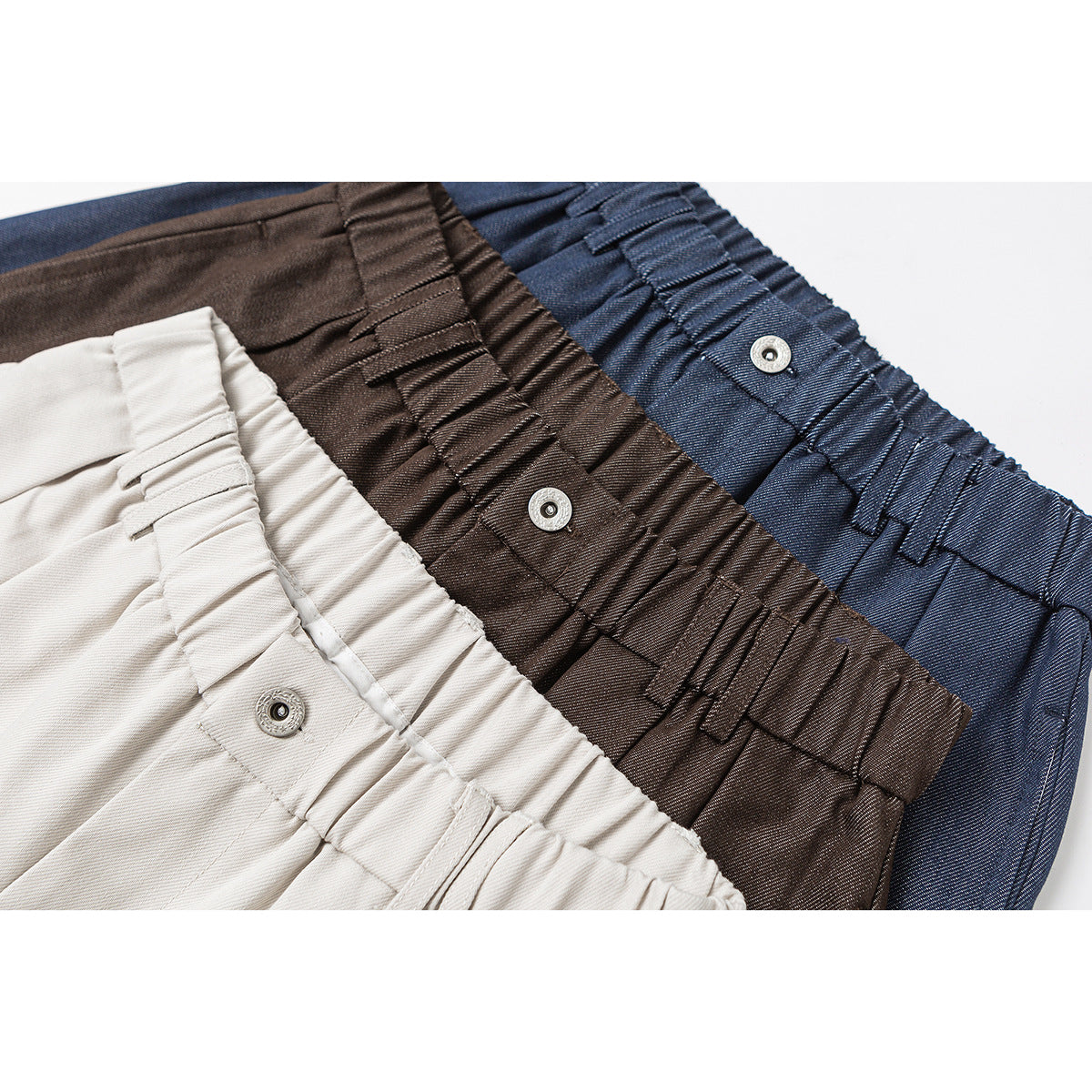 Close-up of gathered waistbands and snap closures on cream, brown, and navy wide-leg shorts.