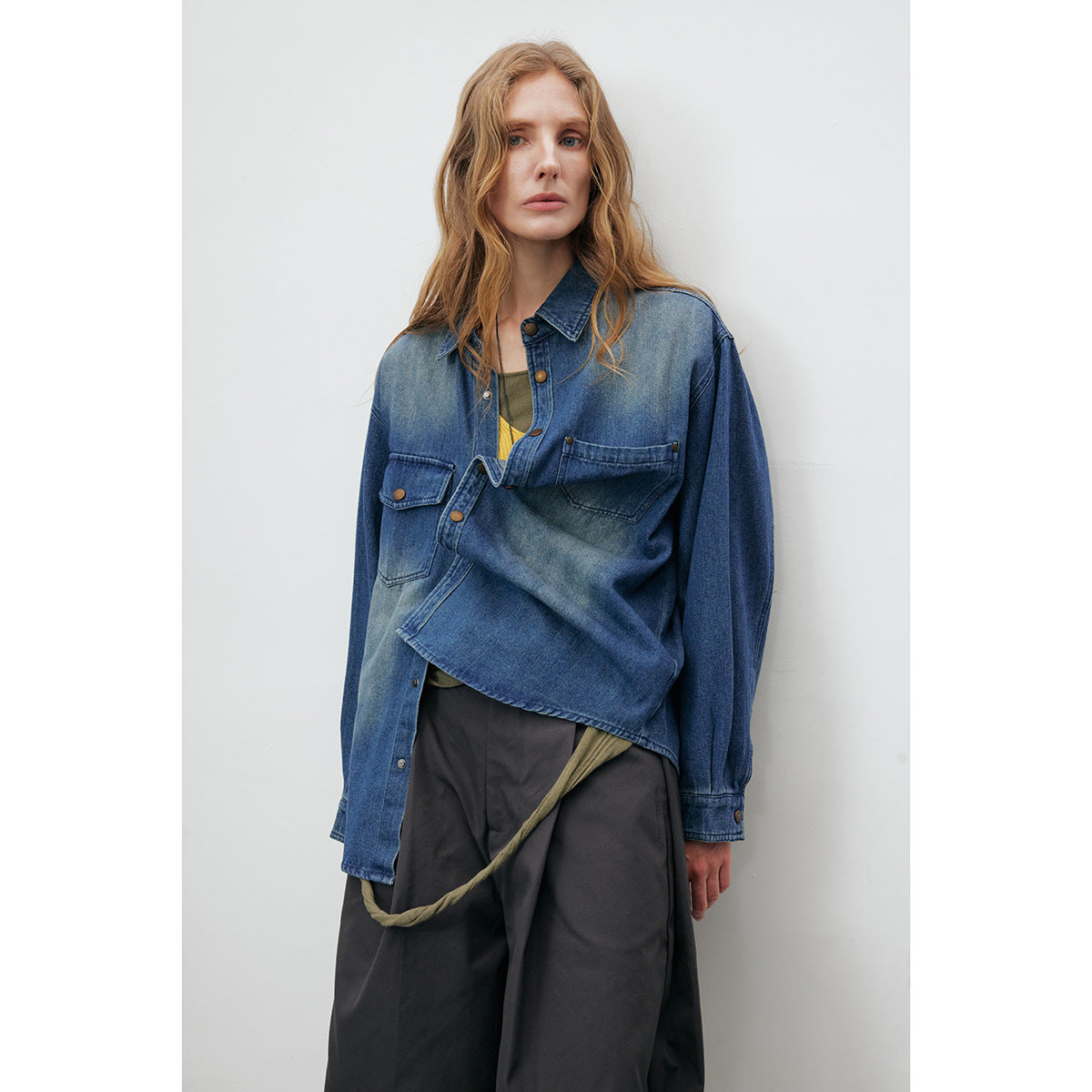Model wearing an oversized blue denim shirt, with one front panel folded across the torso.