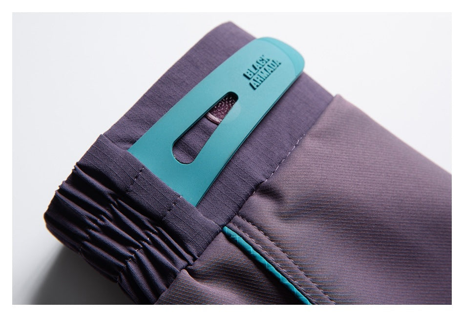 Close-up of purple pants waistband with gathered elastic, teal trim, and a turquoise clip.