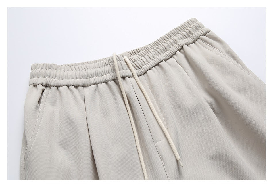 Close-up of light beige joggers showing the gathered elastic waistband, drawstrings, and front pocket seam.