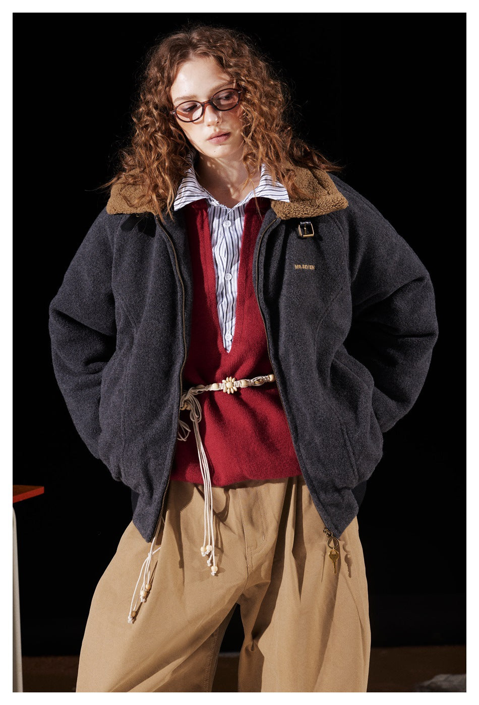 Model wearing a charcoal zip jacket with a tan fleece collar over a red sweater and striped shirt.