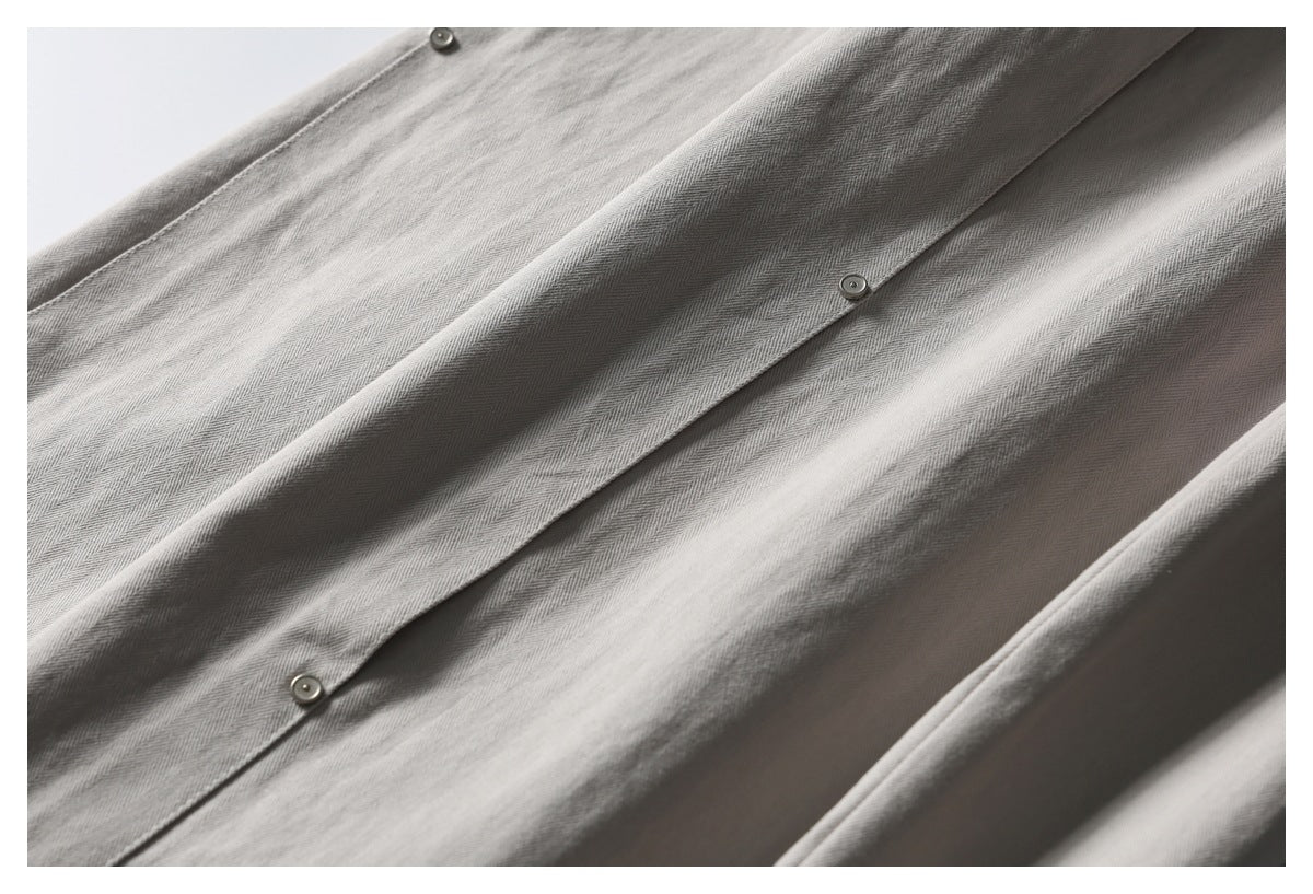 Close-up of light gray-beige fabric with a diagonal placket fastened by several metal snaps.