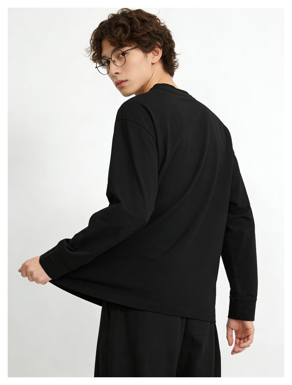 Man in black long-sleeve top seen from the back, looking over his shoulder and pulling the sleeve hem