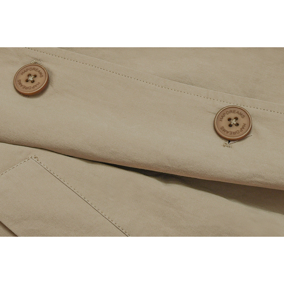 Close-up of two brown buttons embossed with English lettering on a beige coat.