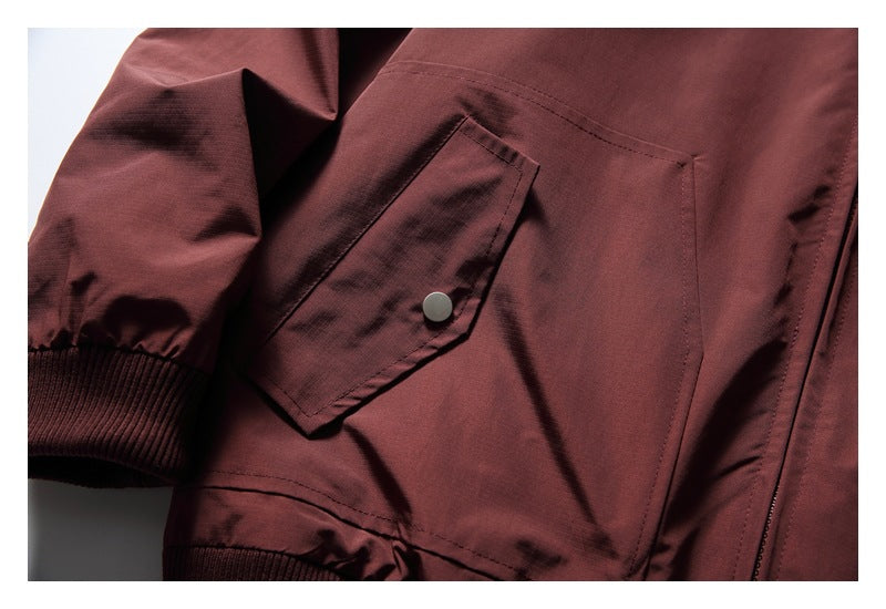 Close-up of a burgundy jacket's snap-fastened flap pocket, sleeve cuff, and ribbed hem.