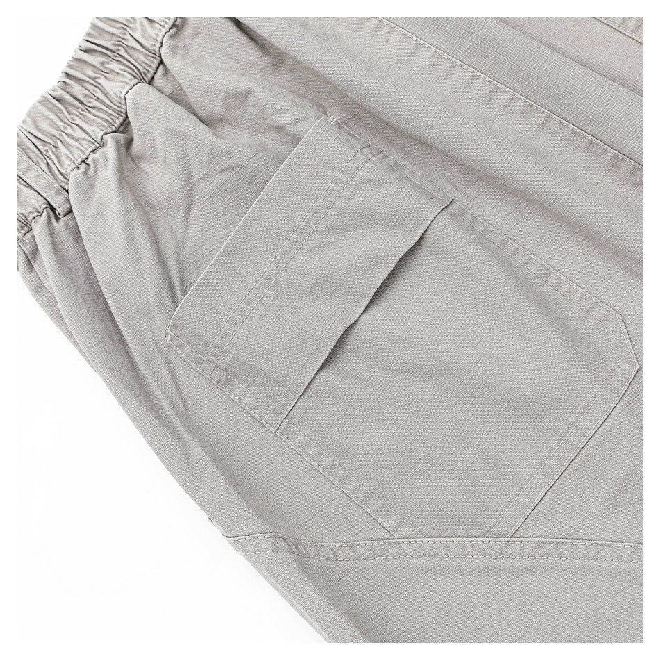 Angled close-up of a large patch pocket and gathered waistband on gray trousers.