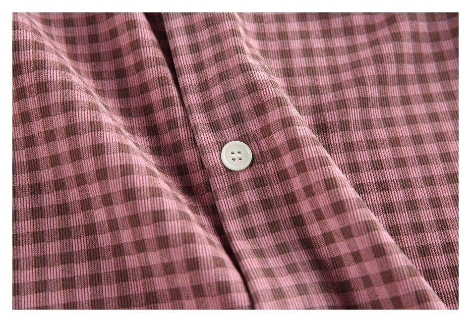 Close-up of a white shirt button against dusty pink and brown checked fabric.