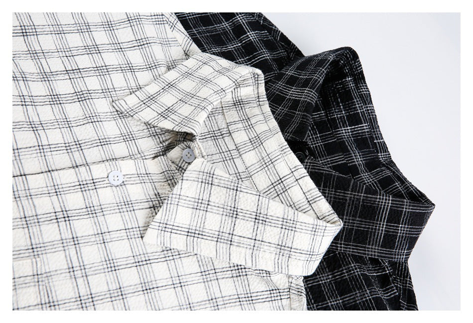 Close-up of overlapping ivory and black plaid button-up shirts, showing their collars, sleeves, and buttons.
