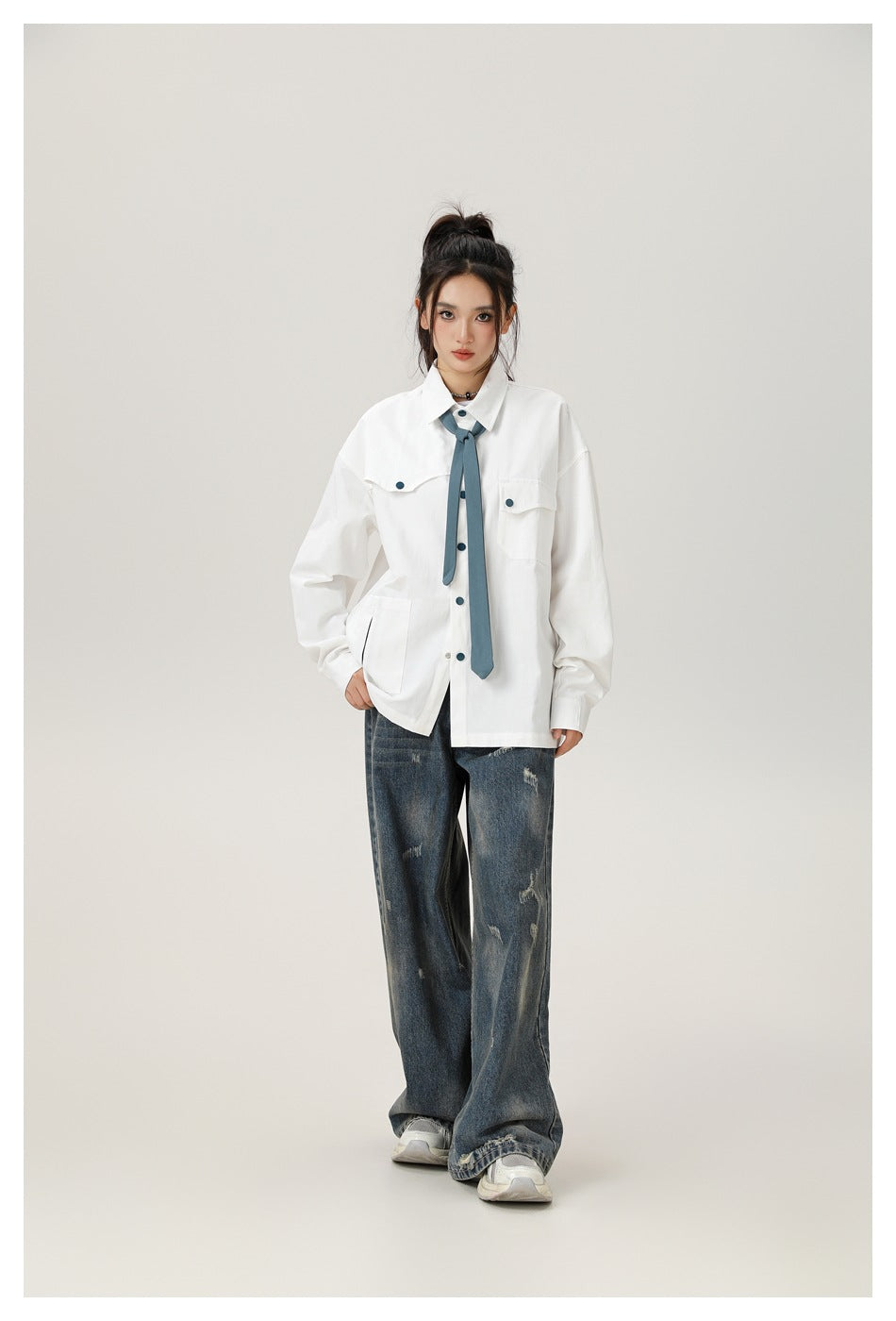 Model wearing a white oversized button-up shirt with flap pockets and a blue necktie, paired with distressed wide-leg jeans.