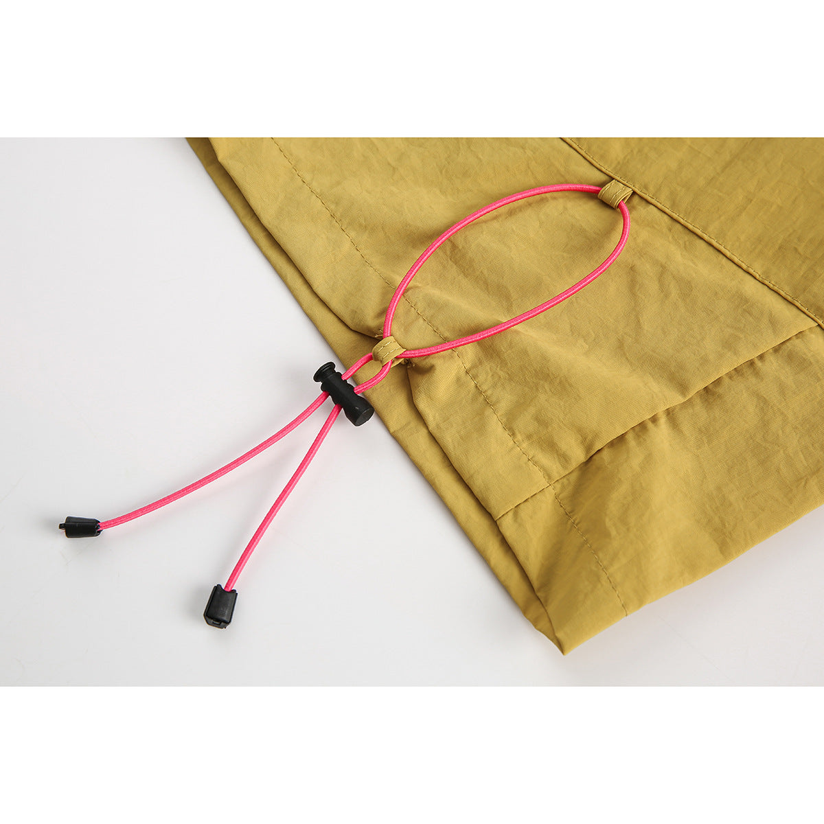 Close-up of mustard shorts with a bright pink adjustable cord and black cord lock near the hem.