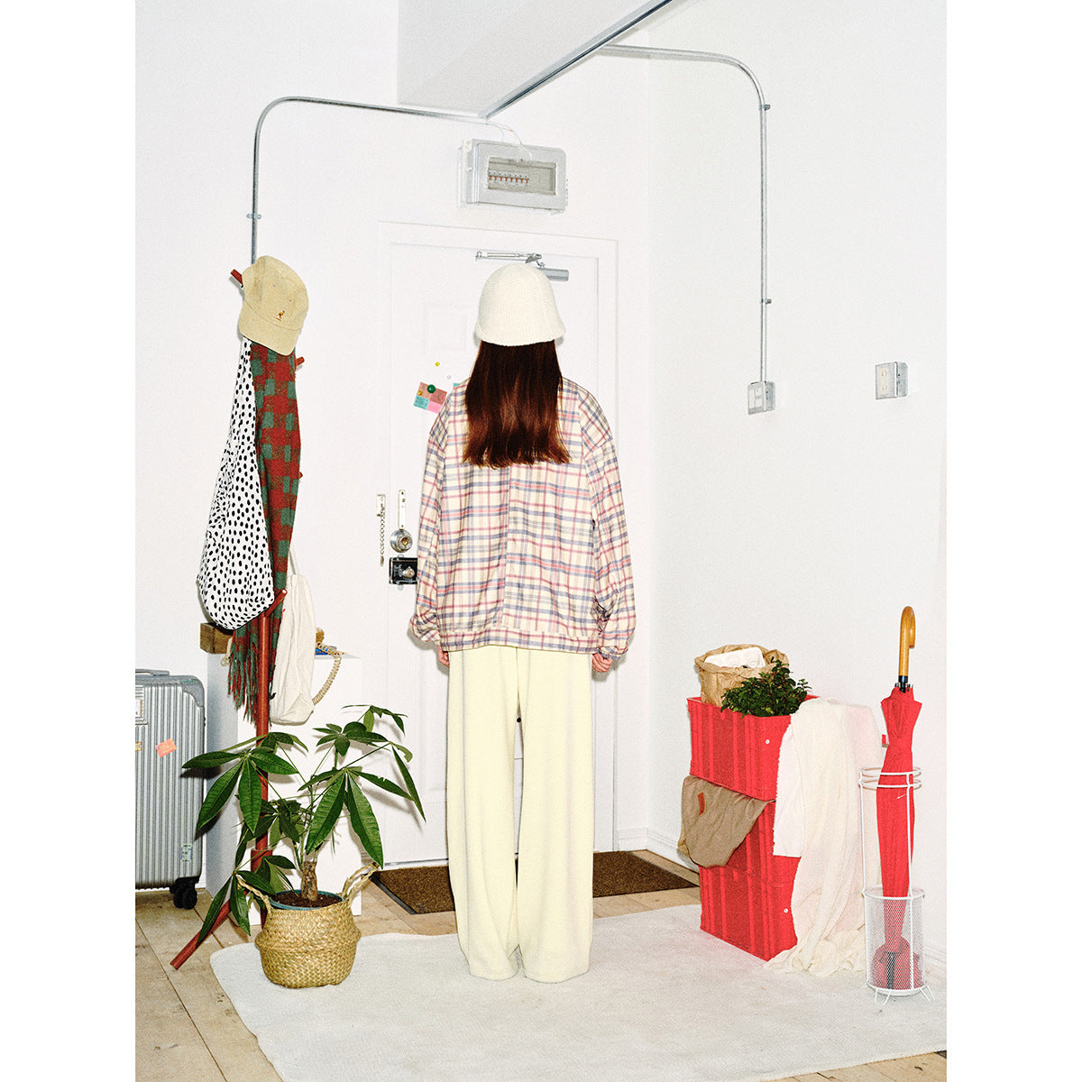Back view of a model wearing a pastel plaid jacket with elastic cuffs and hem, cream pants, and a white bucket hat.