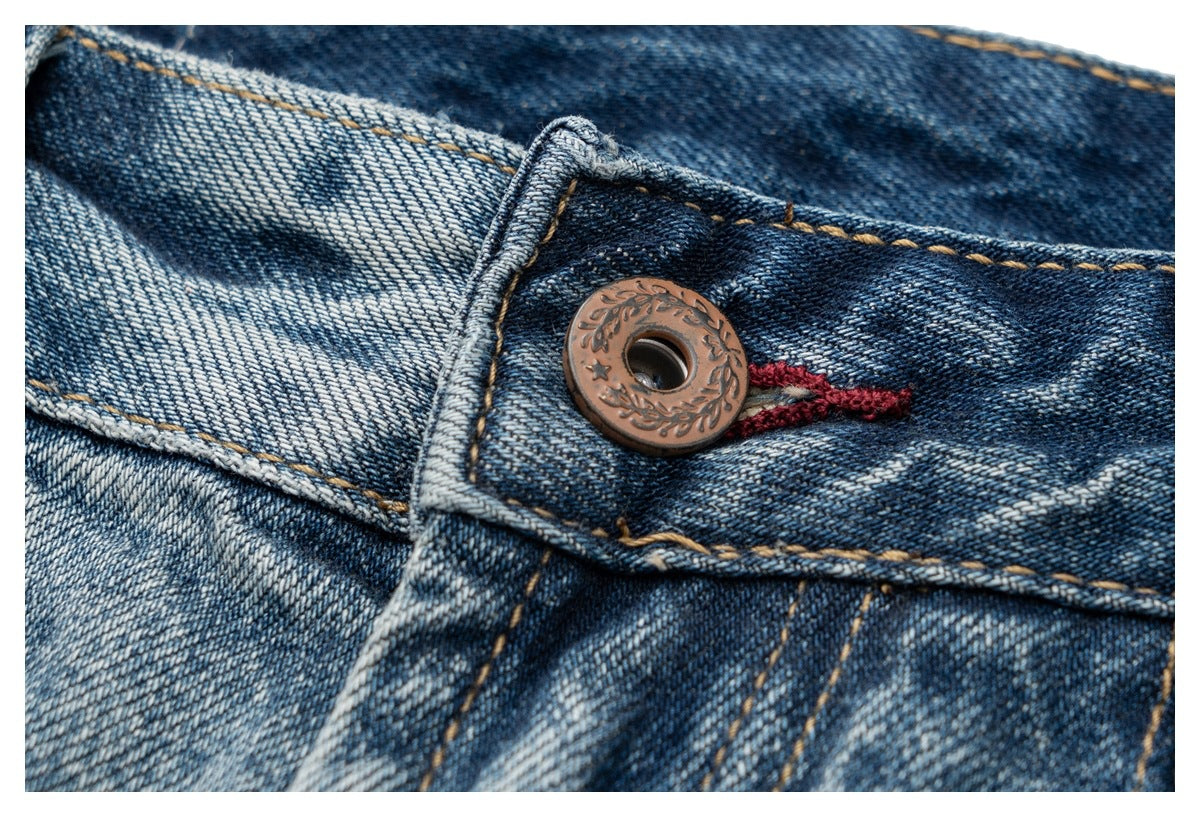 Close-up of a bronze decorative button and red buttonhole on faded blue denim.