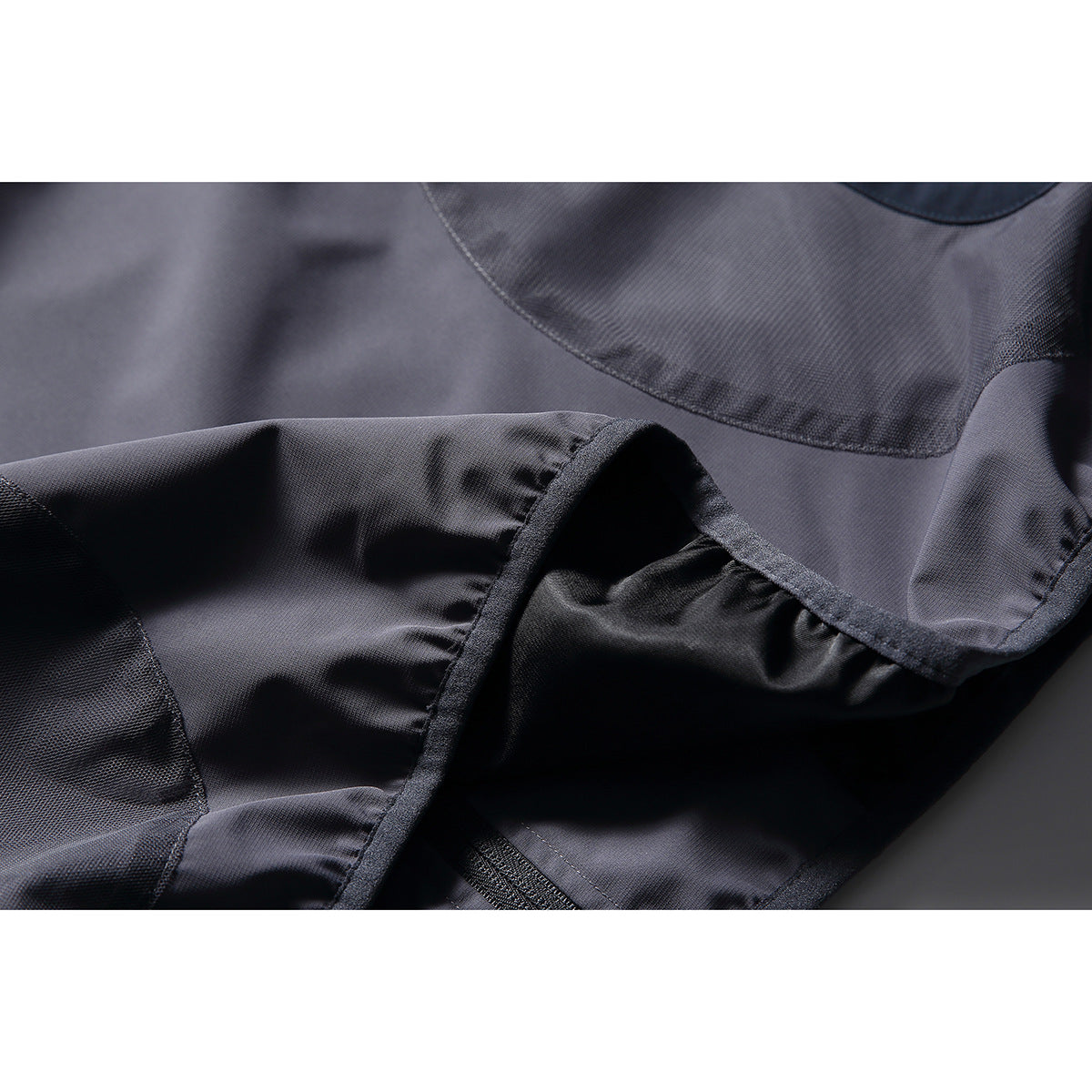 Close-up of the jacket's dark fabric, curved panel seam, and stitched edge.