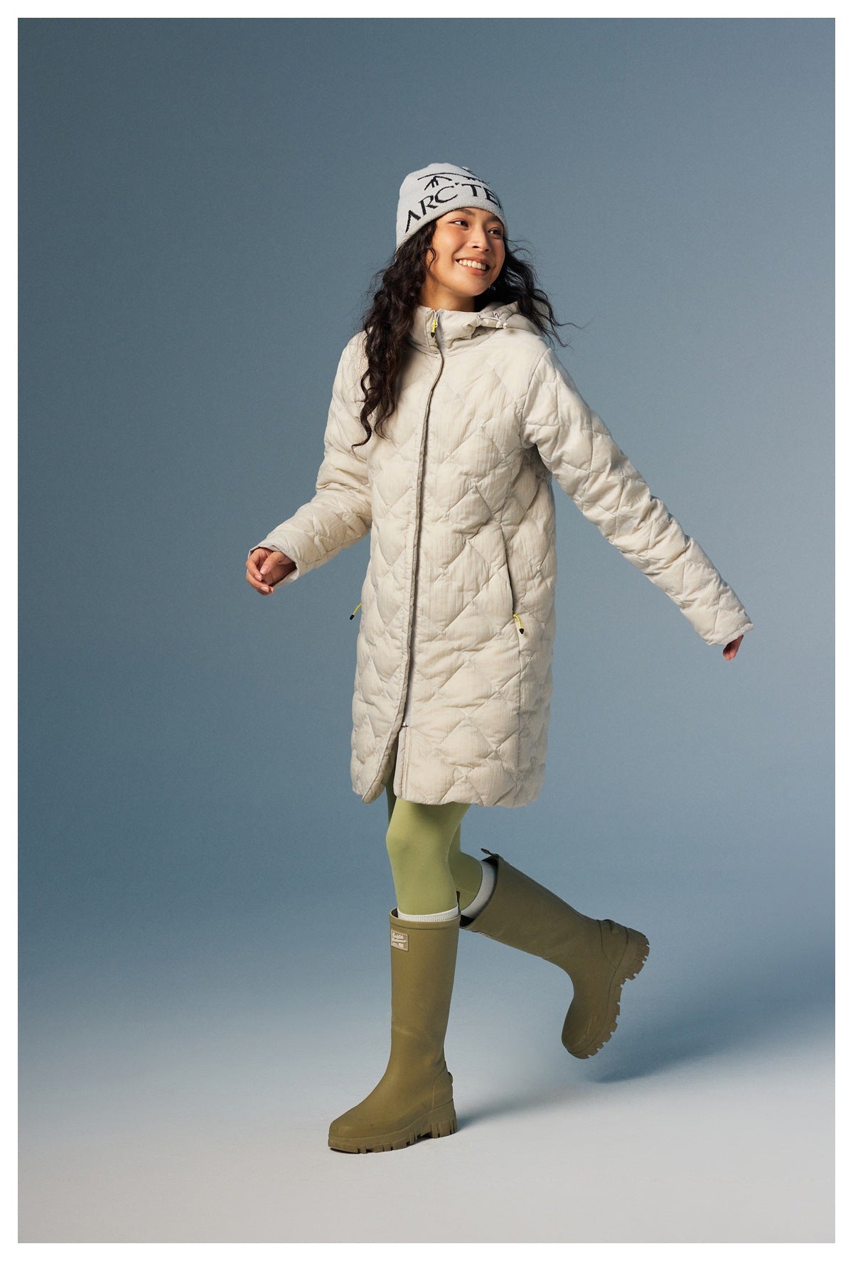 Model wearing a cream diamond-quilted hooded coat, shown from the front with arms outstretched.