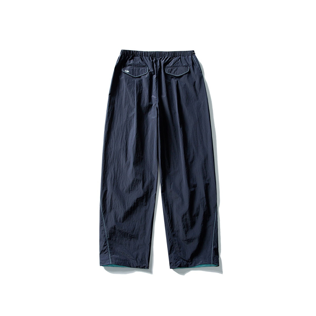 Back view of dark navy loose-fitting pants with an elastic waist, two flap pockets, and contrast trim, displayed flat on