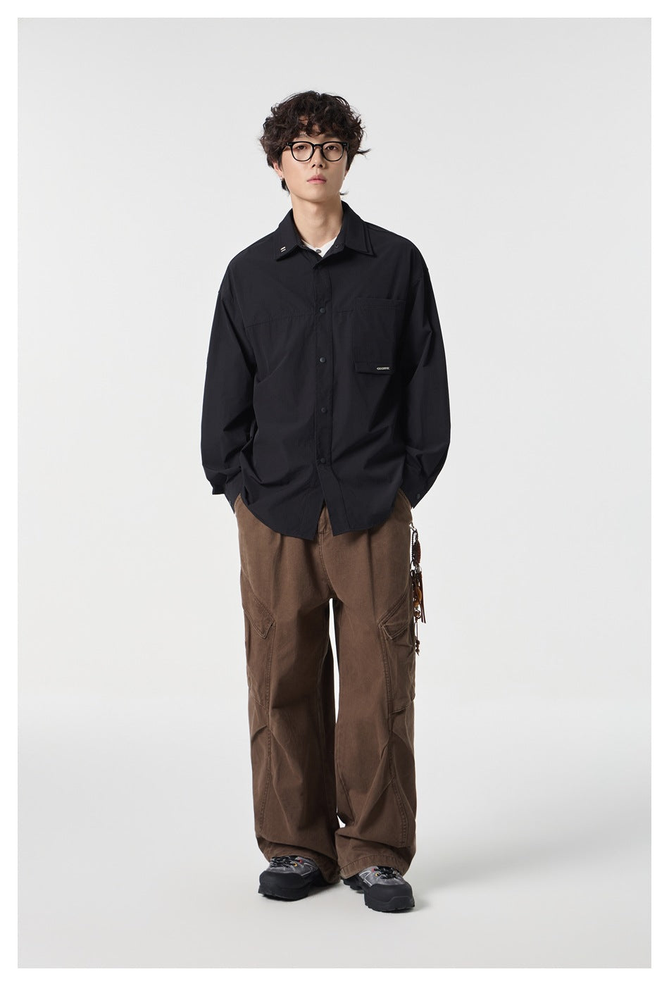 Full-length model wearing a black oversized button-front shirt with brown cargo trousers.