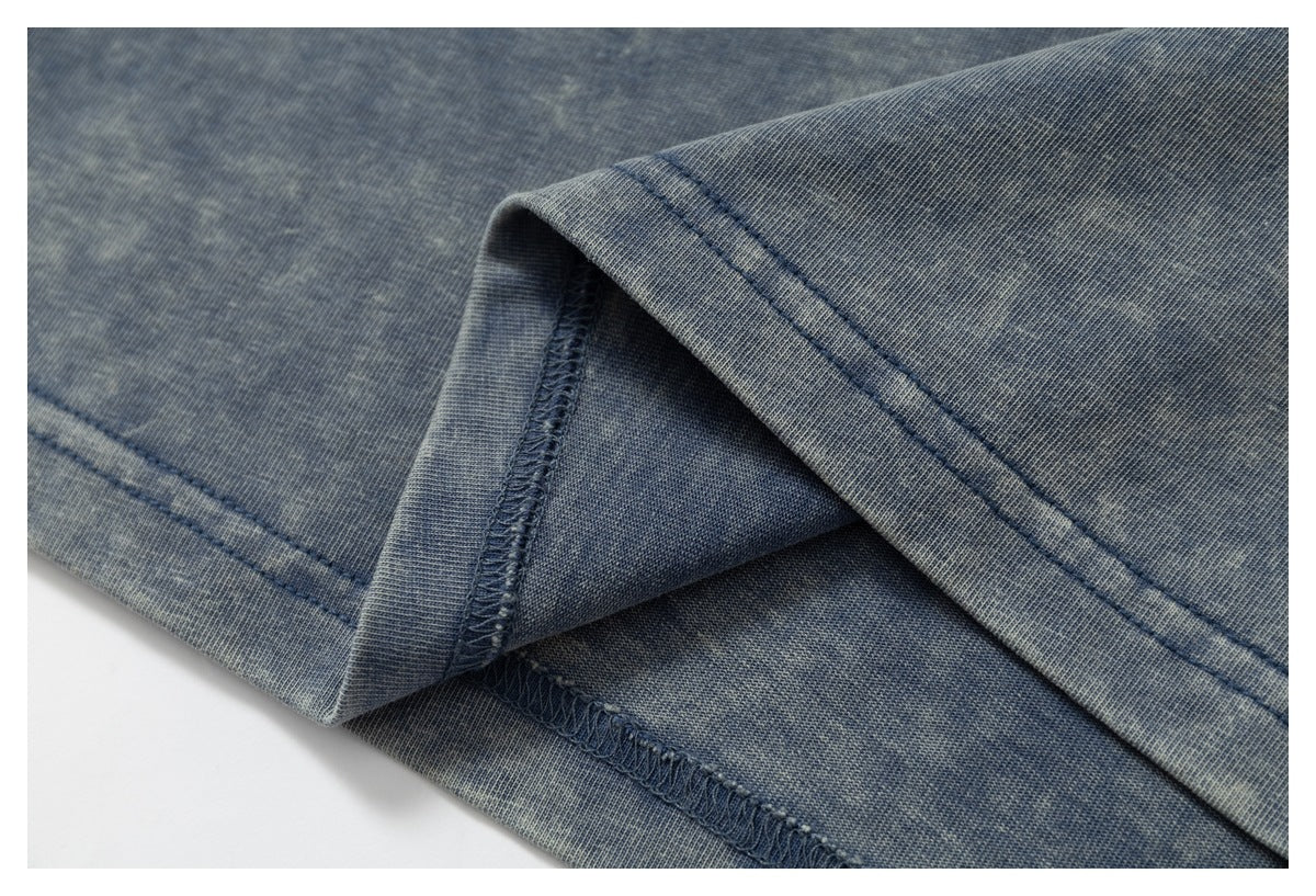 Close-up of blue-gray garment fabric showing a folded hem, double stitching, and an overlocked seam.