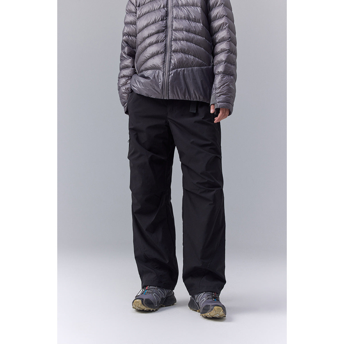 Front view of a person wearing loose black pants with articulated knees, beneath a gray quilted jacket.