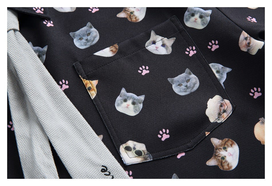 Close-up of a square chest pocket on a black shirt printed with cat faces and pink paw prints.
