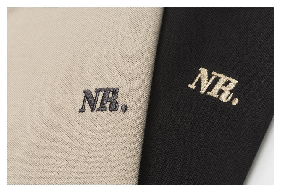 Close-up of embroidered NB logos on beige and black polo shirt fabric.