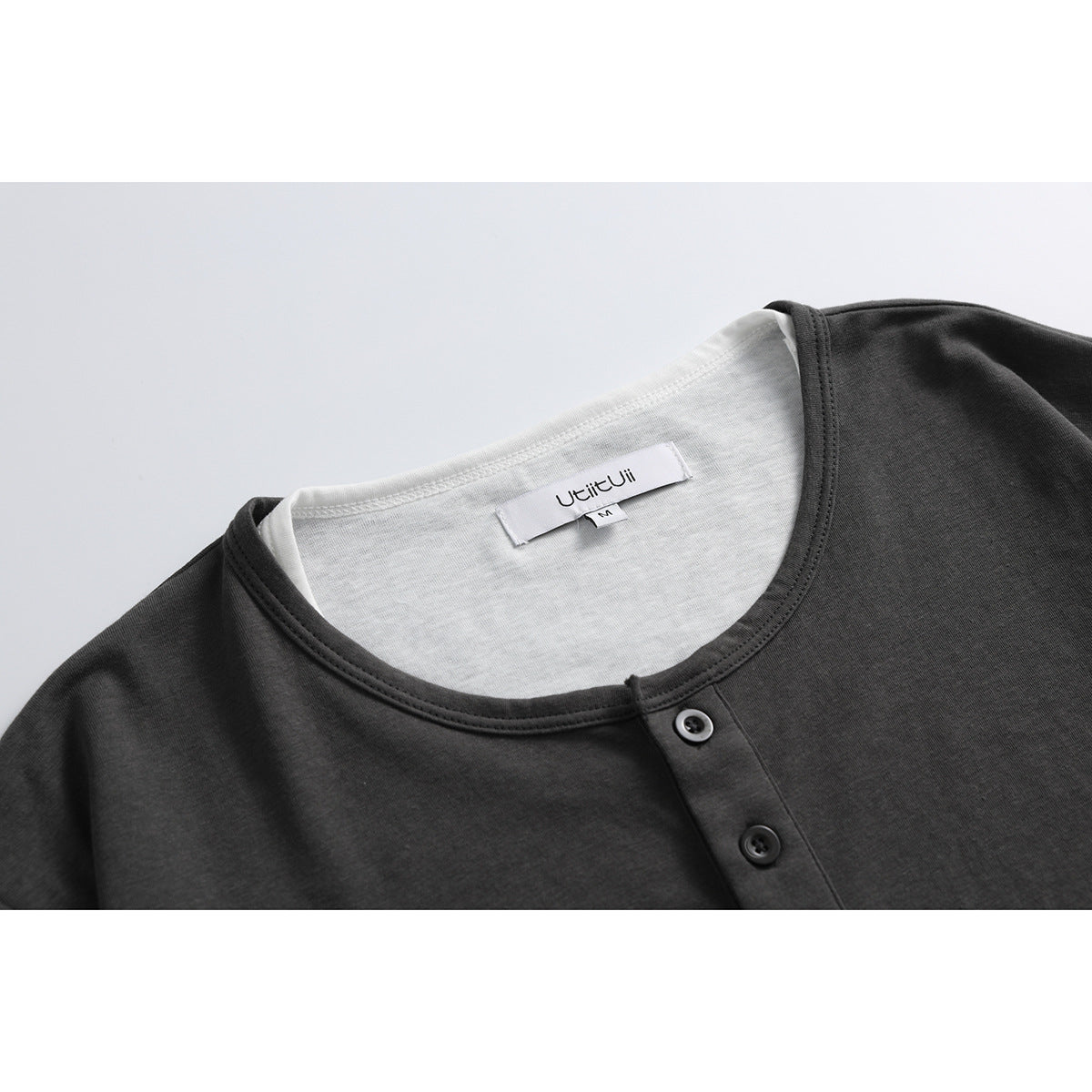 Close-up of a charcoal short-sleeve shirt's crew neck and two-button placket, with a white neck label.