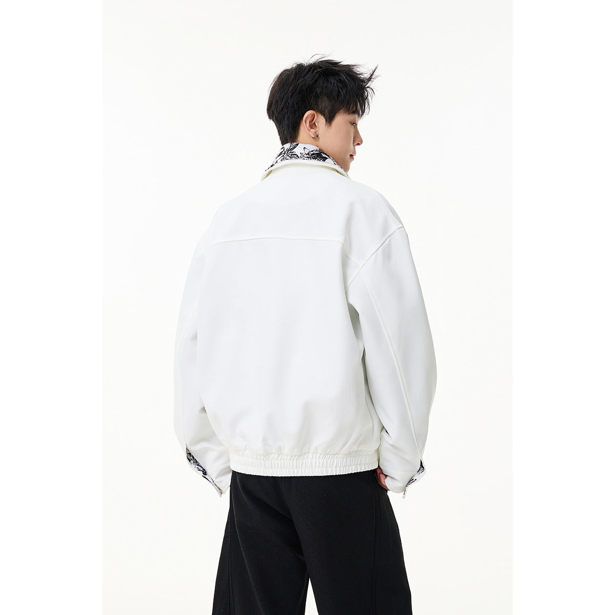 Back view of a model wearing a white jacket with a gathered hem and black trousers.