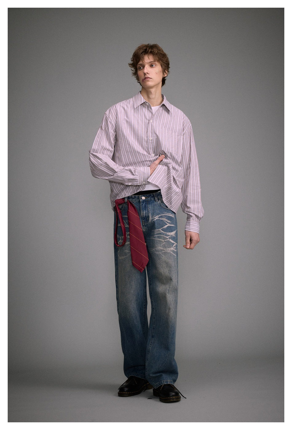 Model wearing loose blue jeans with pale abstract thigh designs and a pink-and-white striped shirt.