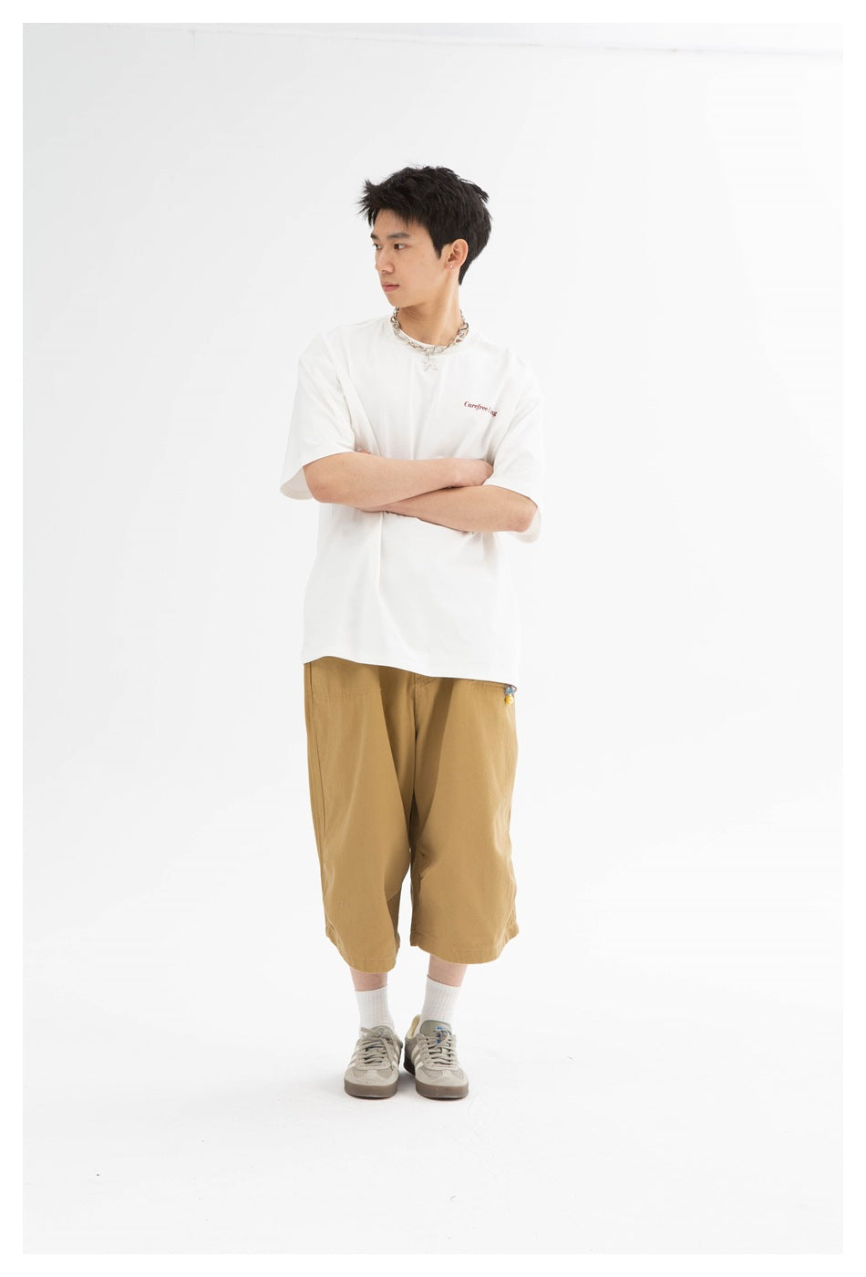 Person wearing a white relaxed T-shirt with small red chest print, arms crossed, with khaki cropped pants