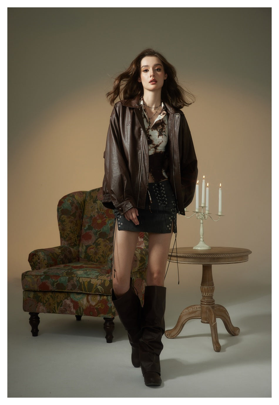 Model walking in coffee brown zip-front faux-leather jacket with printed top, black mini skirt and tall brown boots